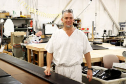 Inmate standing by sewing table at sewing shop.