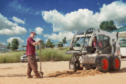 Inmates operating heavy machinery to dig hole to install volleybal post