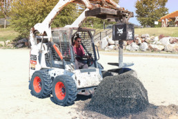 Inmates operating heavy machinery to dig hole to install volleybal post